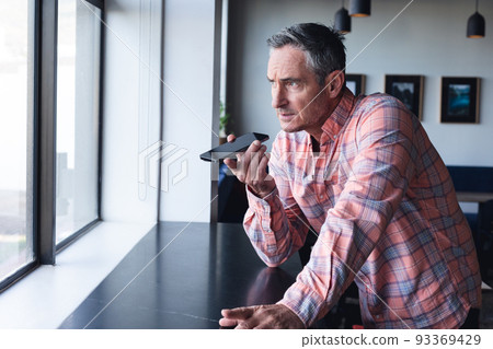 Caucasian mature businessman talking on smart phone speaker by window at creative office 93369429