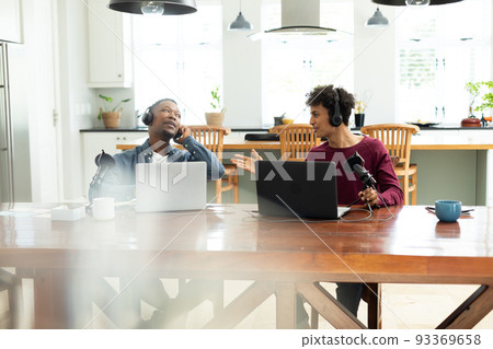 Multiracial young male workers wearing headphones and talking while recording podcast in office Multiracial young male workers wearing headphones and talking while recording podcast in office 93369658