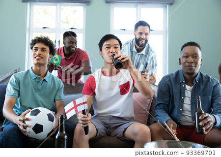 Happy multiracial male friends with ball and beer bottles watching soccer match on sofa at home 93369701