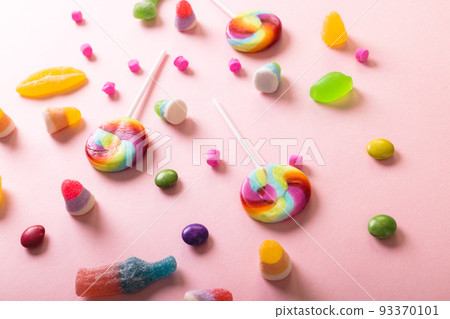 High angle view of multi colored sugar candies and lollipops scattered over pink background 93370101