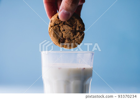 Cropped hand of person dipping cookie in milk against blue background, copy space Cropped hand of person dipping cookie in milk against blue background, copy space 93370234