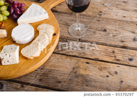 High angle view of various cheese with grapes and red wine on wooden table, copy space 93370297