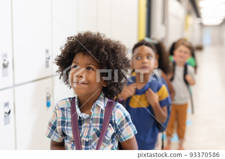 Multiracial innocent elementary school children standing in row by lockers 93370586