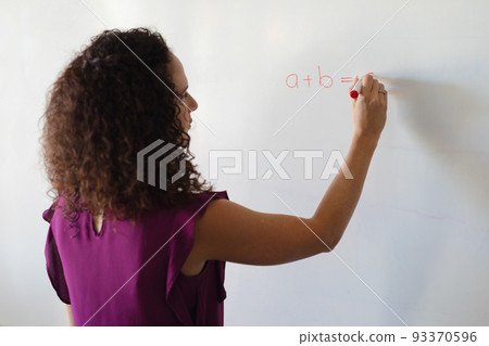 Caucasian young female teacher writing formula on whiteboard during math class in school 93370596