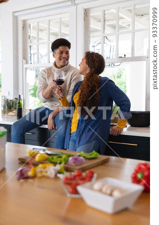 Happy biracial couple preparing food and drinking red wine in kitchen 93370999