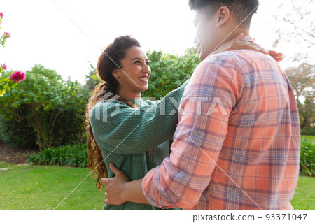 Happy biracial couple embracing and smiling on terrace in garden 93371047