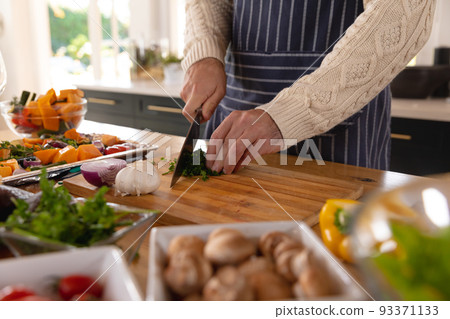 Midsection of caucasian man preparing food, chopping vegetables wearing apron in kitchen 93371133