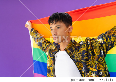 Happy biracial man holding lgbt rainbow flag and smiling on purple background Happy biracial man holding lgbt rainbow flag and smiling on purple background 93371414