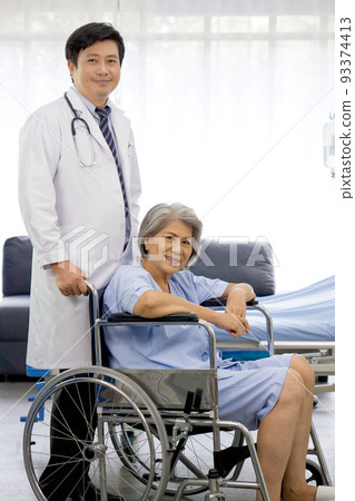Portrait of asian doctor with stethoscope and gown push a wheelchair of the elderly patient. Healthcare and medicine concept. 93374413