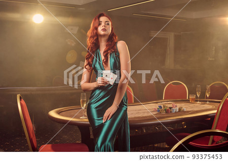 Young beautiful woman is posing against a poker table in luxury casino. Young beautiful woman is posing against a poker table in luxury casino. 93375453