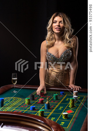 Young blonde woman wearing beautiful sexy shiny dress is playing roulette in the casino 93375498