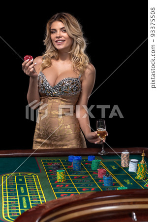 Young blonde woman wearing beautiful sexy shiny dress is playing roulette in the casino 93375508