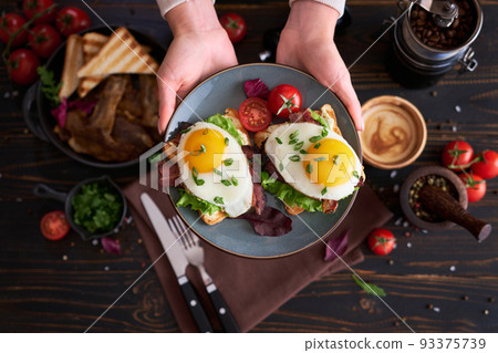 Tasty breakfast - fried egg toasts, bacon, tomatoes on wooden kitchen table Tasty breakfast - fried egg toasts, bacon, tomatoes on wooden kitchen table 93375739