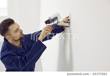 Male technician installs video surveillance camera on wall inside office for security. 93375981
