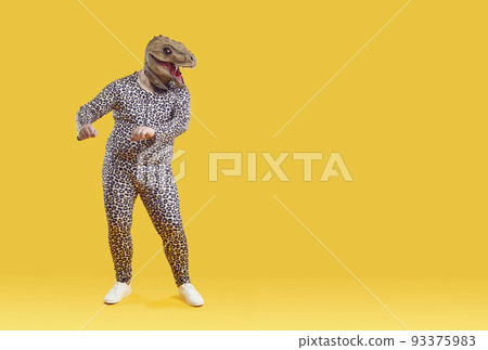 Funny eccentric overweight man dancing in strange dinosaur rubber mask on orange background. 93375983