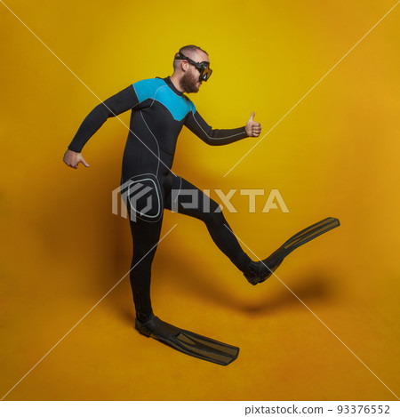 Traveling concept. Happy diver in a mask and fins going somewhere against yellow studio background 93376552