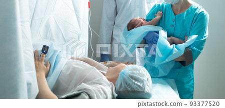 Nurse holds newborn baby close to mother in hospital 93377520