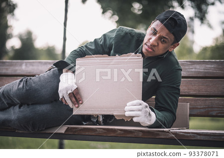 Man reclining on bench showing cardboard to camera Man reclining on bench showing cardboard to camera 93378071