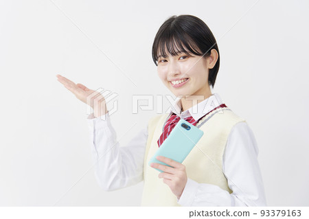 A high school girl holding a smartphone on a white background and pointing to the left with her palm A high school girl holding a smartphone on a white background and pointing to the left with her palm 93379163