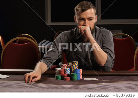 Handsome bearded man is playing poker sitting at the table in casino. 93379339