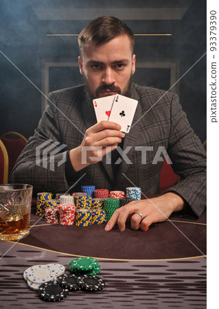 Handsome bearded man is playing poker sitting at the table in casino. 93379390
