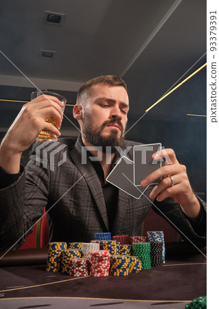 Handsome bearded man is playing poker sitting at the table in casino. 93379391
