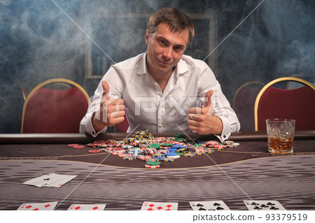Handsome emotional man is playing poker sitting at the table in casino. 93379519
