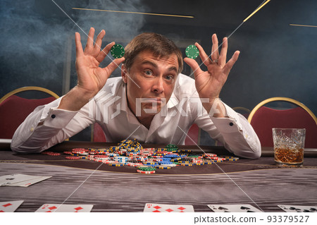 Handsome emotional man is playing poker sitting at the table in casino. Handsome emotional man is playing poker sitting at the table in casino. 93379527