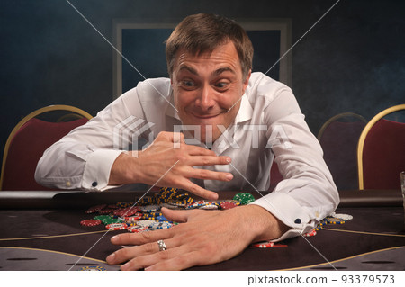Handsome emotional man is playing poker sitting at the table in casino. 93379573