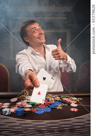 Handsome emotional man is playing poker sitting at the table in casino. 93379626