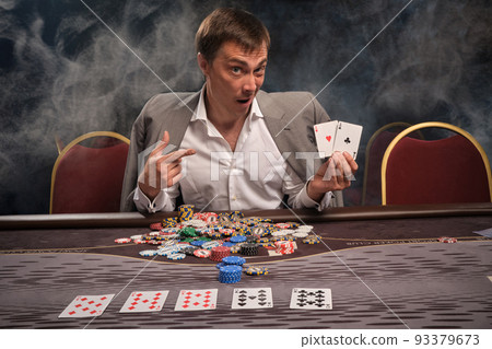 Handsome emotional man is playing poker sitting at the table in casino. 93379673