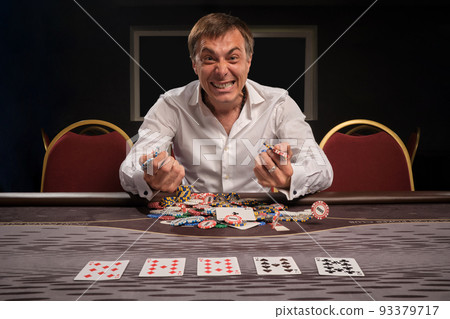 Handsome emotional man is playing poker sitting at the table in casino. 93379717
