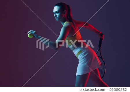 Young woman, professional tennis player training isolated on blue background in neon. 93380282