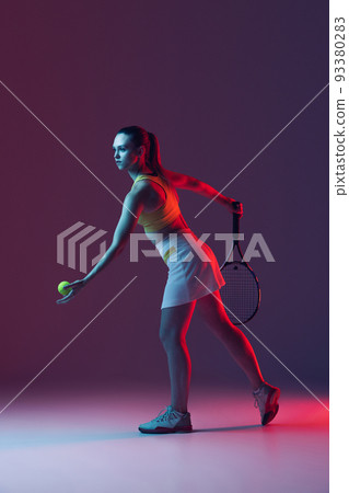 Full length portrait of young woman playing tennis isolated on dark background in neon. Healthy lifestyle, fitness, sport, exercise concept. 93380283