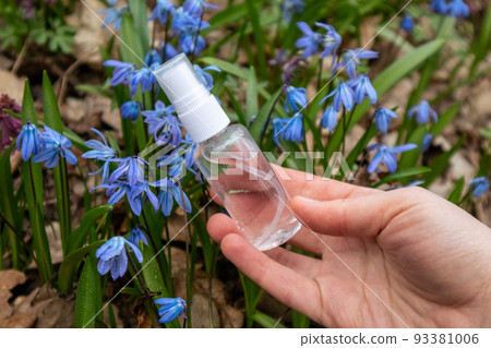 Hand holding clear spray bottle in blue flowers Hand holding clear spray bottle in blue flowers 93381006