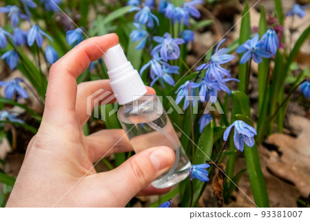 Hand spray clear drops from bottle in blue flowers Hand spray clear drops from bottle in blue flowers 93381007