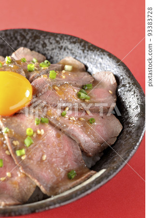 Roast beef rice bowl topped with raw egg yolk, green onion, and white sesame seeds 93383728