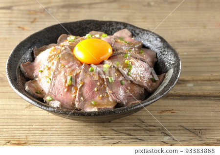 Roast beef rice bowl topped with raw egg yolk, green onion, and white sesame seeds 93383868