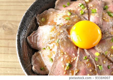 A bird's-eye view of a roast beef bowl topped with raw egg yolk, all-purpose green onions, and white sesame seeds A bird's-eye view of a roast beef bowl topped with raw egg yolk, all-purpose green onions, and white sesame seeds 93384007