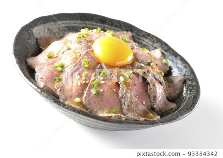 Roast beef bowl topped with raw egg yolk, all-purpose green onions, and white sesame, photographed against a white background 93384342
