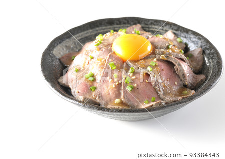Roast beef bowl topped with raw egg yolk, all-purpose green onions, and white sesame, photographed against a white background 93384343
