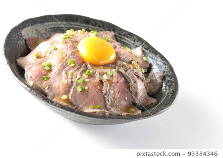 Roast beef bowl topped with raw egg yolk, all-purpose green onions, and white sesame, photographed against a white background Roast beef bowl topped with raw egg yolk, all-purpose green onions, and white sesame, photographed against a white background 93384346