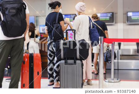 Two woman passengers with face mask check in at the airport. Two woman passengers with face mask check in at the airport. 93387140