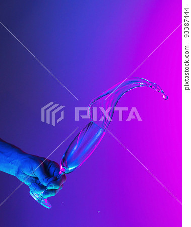 Authentic hand pouring pure water splash from wine or champagne glass over bright blue-pink gradient background in neon light. Art, drinks, creativity Authentic hand pouring pure water splash from wine or champagne glass over bright blue-pink gradient background in neon light. Art, drinks, creativity 93387444