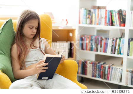A young girl is reading a book while sitting in a bright yellow armchair in a public library. The concept of home education, recreation, mindfulness. The girl is wearing light clothes , side view . A young girl is reading a book while sitting in a bright yellow armchair in a public library. The concept of home education, recreation, mindfulness. The girl is wearing light clothes , side view . 93389271
