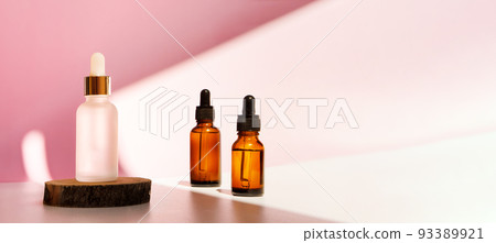 Banner of three transparent amber and frozen glass dropper bottles on pink background in the sunlight. Wooden podium. Pipette with fluid hyaluronic acid, serum, retinol. Cosmetics, healthcare, beauty  93389921