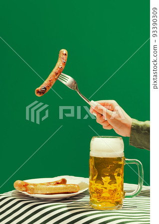 Beer and fried frankfurter. Human hand with mug of cold frothy beer over dark green background. Oktoberfest, vacation, happiness, festival and ad concept. Beer and fried frankfurter. Human hand with mug of cold frothy beer over dark green background. Oktoberfest, vacation, happiness, festival and ad concept. 93390309