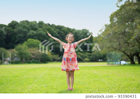 在陽光明媚的公園裡張開雙臂的微笑女孩 在陽光明媚的公園裡張開雙臂的微笑女孩 93390431