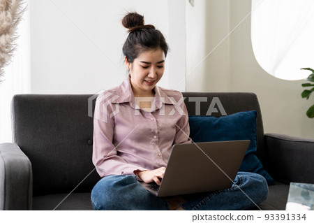 Smiling asian young woman working on laptop at home office. Young asian student using computer remote studying, virtual training, e-learning, watching online education webinar at house 93391334