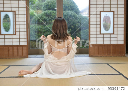 一位身穿白色內衣的年輕女子坐在一座古老民居的日式房間裡的背影 93391472